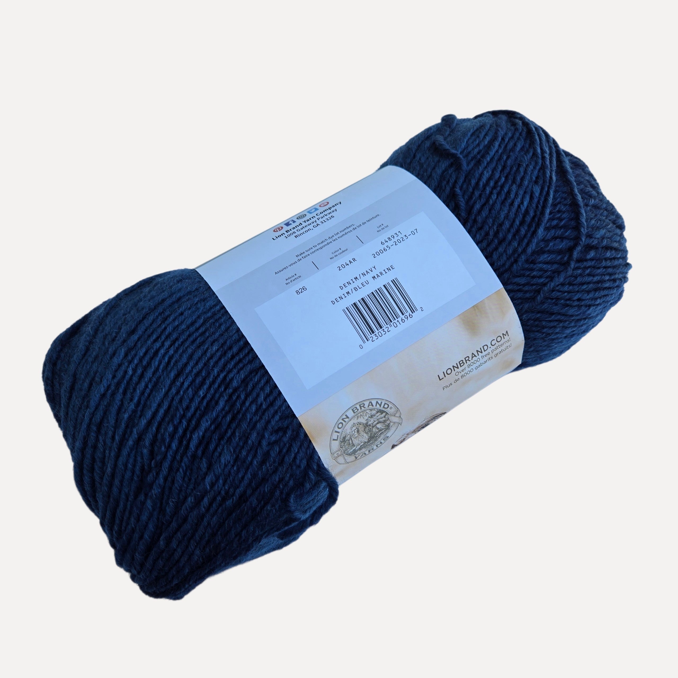 A skein of dark navy blue yarn with a light blue paper label, photographed on a clean, solid off-white background.